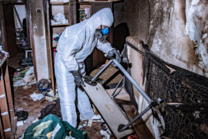 a specialist  in a protective suit from a cleaning company cleans a destroyed housing after a fire